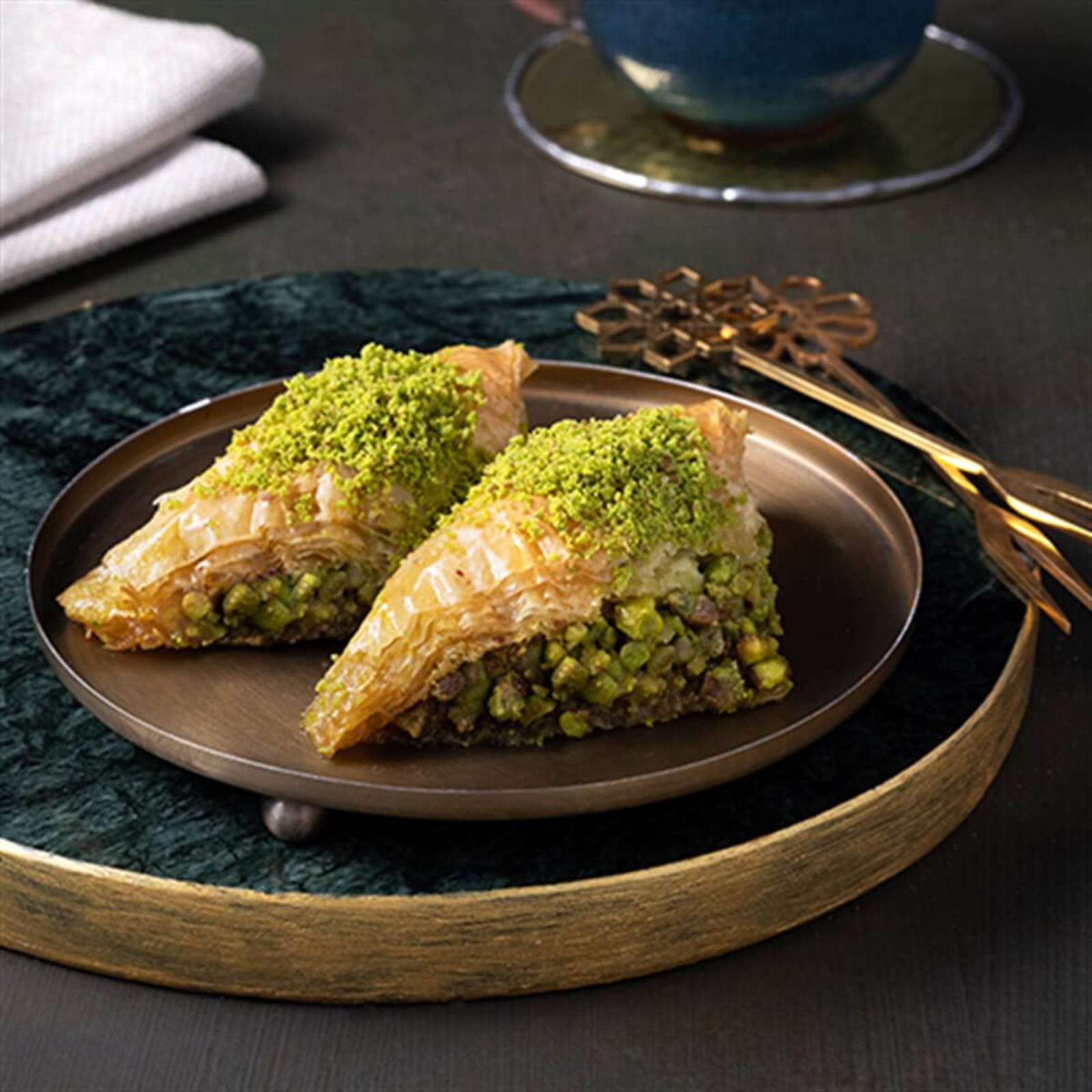 Two pieces of baklava with green pistachio filling on a plate, served with a cup of tea.